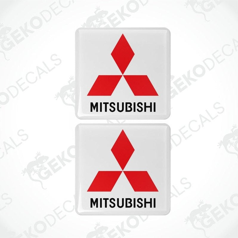 Two white vinyl stickers with a red Mitsubishi logo on each, placed against a black background with the text 'MITSUBISHI' below each sticker.