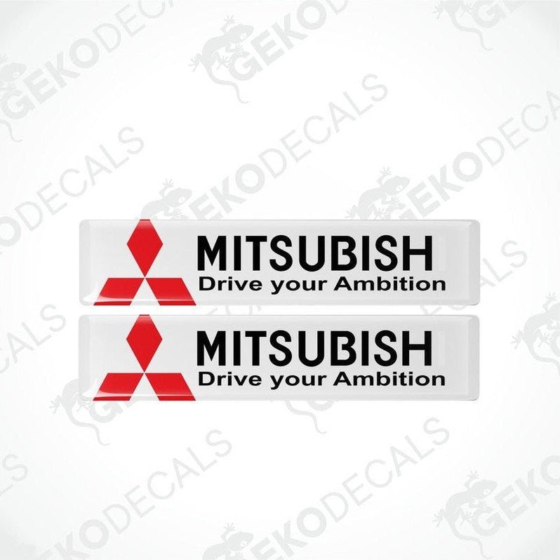 Two rectangular white vinyl decals with the Mitsubishi logo and the text 'MITSUBISHI Drive your Ambition' in black and red.