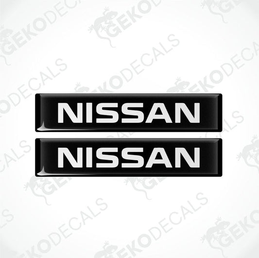Two black rectangular car decals with the text 'NISSAN' in white uppercase letters