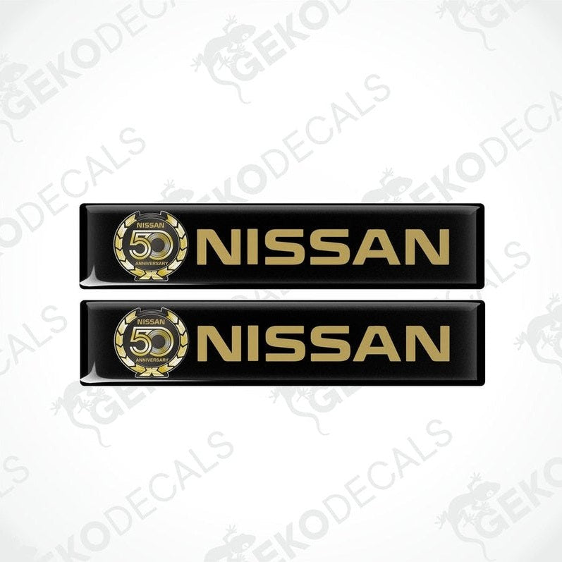 Two black vinyl stickers with gold and white text and graphics representing the NISSAN brand, placed against a white background.