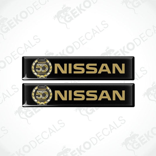 Two black vinyl stickers with gold and white text and graphics representing the NISSAN brand, placed against a white background.