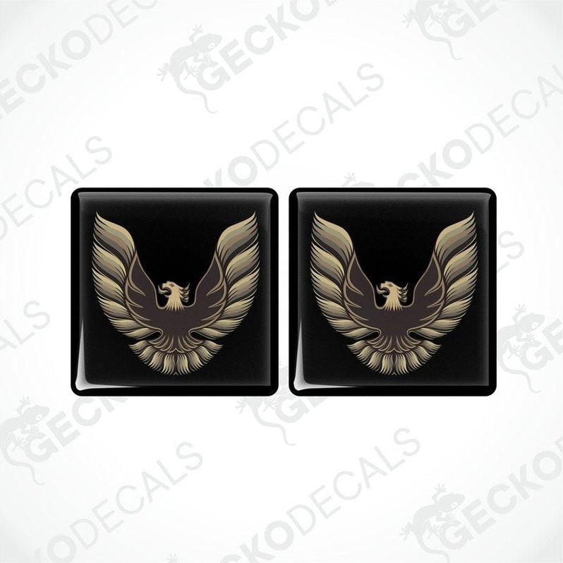 Two black vinyl stickers with a gold and bronze emblem design, placed against a white background.
