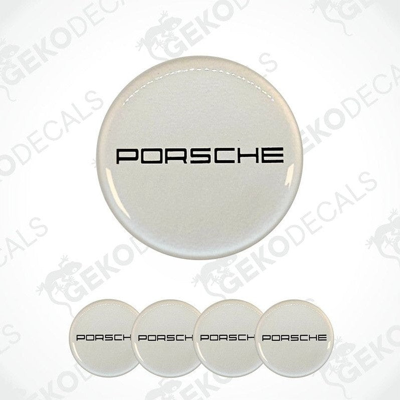 A set of four white vinyl stickers with the PORSCHE logo on them. The stickers are designed to be used on car wheel caps.