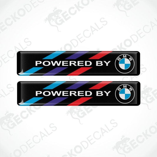 Two vinyl stickers with 'POWERED BY BMW' text and a colorful stripe pattern on a black background.