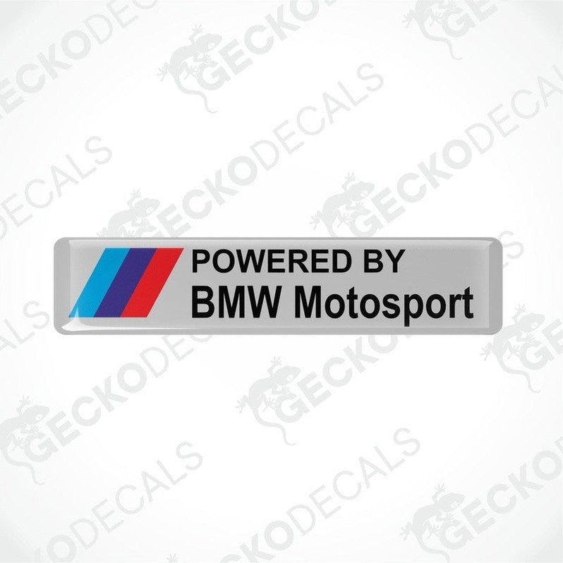 Rectangular white vinyl stickers with the text "POWERED BY BMW MOTORSPORT" with light blue, blue and red BMW logos