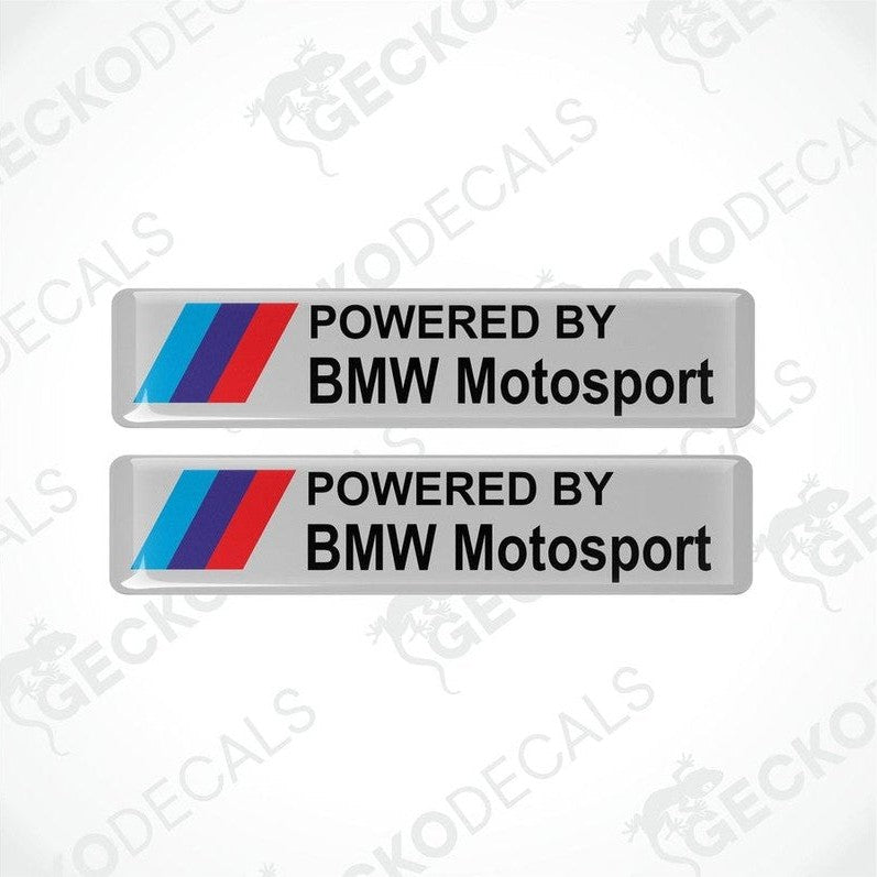 Two rectangular white vinyl stickers with the text "POWERED BY BMW MOTORSPORT" with light blue, blue and red BMW logos
