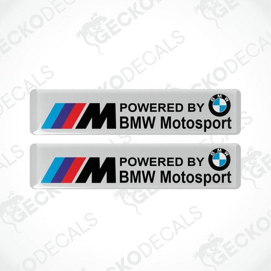 Two white vinyl stickers with the BMW Motosport logo, one featuring the BMW logo alone and the other with the text 'POWERED BY BMW MOTOSPORT M'. Both have a black, red, and white color scheme.