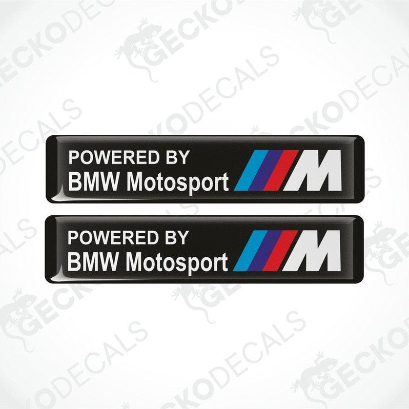 Two black vinyl stickers with the text 'POWERED BY BMW MOTOSPORT M' and the BMW logo in white, red, and blue colors.
