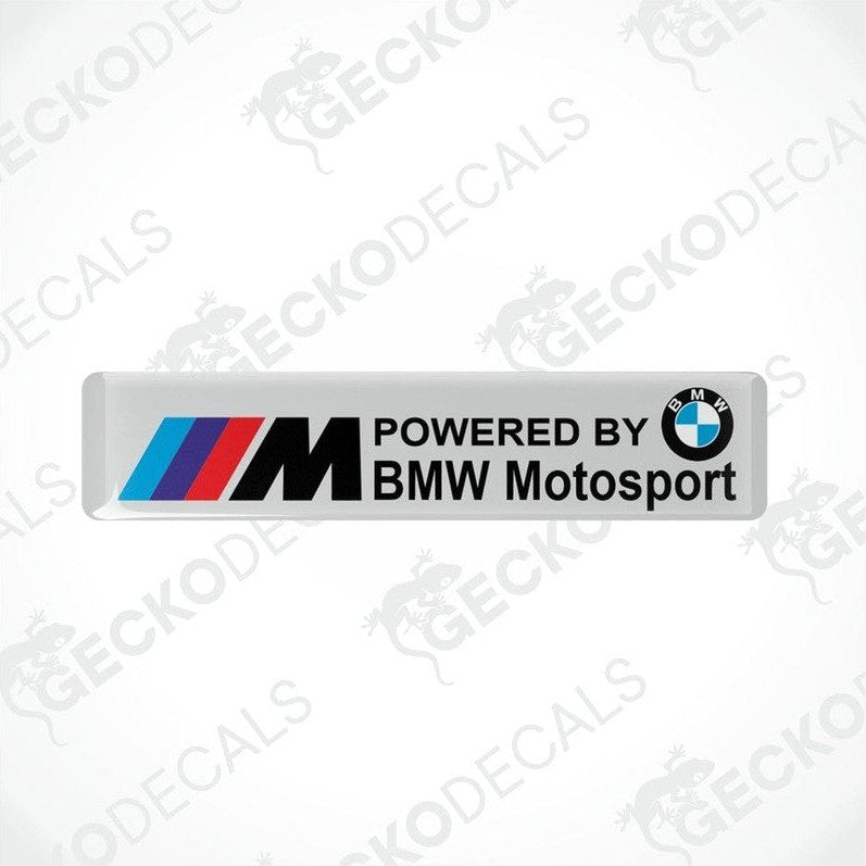 White vinyl stickers with the BMW Motosport logo, one featuring the BMW logo alone and the other with the text 'POWERED BY BMW MOTOSPORT M'. Both have a black, red, and white color scheme.