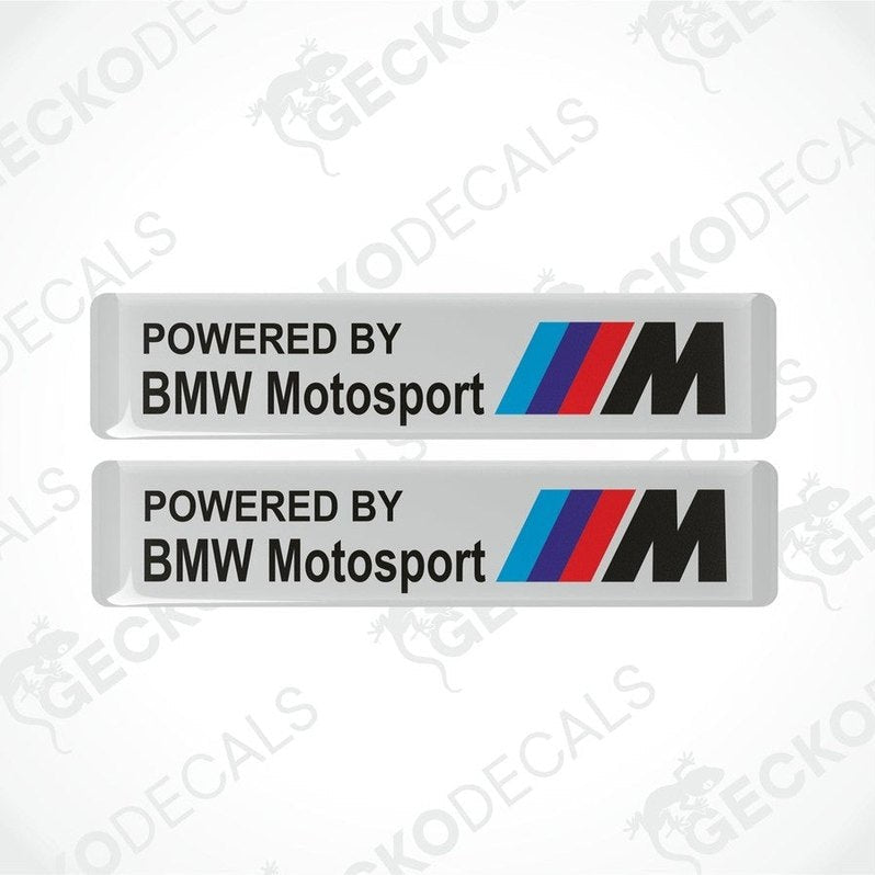 Two white vinyl stickers with the text 'POWERED BY BMW MOTOSPORT M' and the BMW logo in black, red, and blue colors.