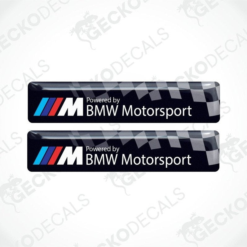 Two vinyl stickers with a  POWERED BY BMW M MOTORSPORT  logo, predominantly black with blue and red checkered pattern.