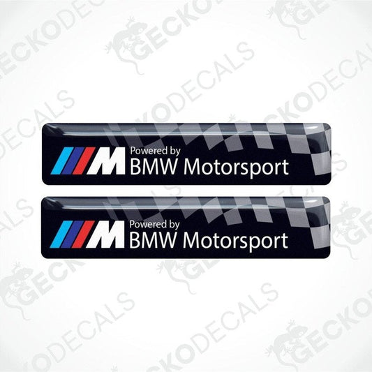 Two vinyl stickers with a  POWERED BY BMW M MOTORSPORT  logo, predominantly black with blue and red checkered pattern.
