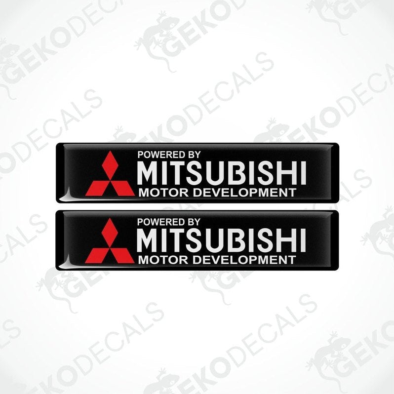 Two rectangular black vinyl decals with the red Mitsubishi logo and the text 'POWERED BY MITSUBISHI MOTOR DEVELOPMENT'.