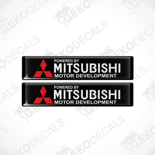 Two rectangular black vinyl decals with the red Mitsubishi logo and the text 'POWERED BY MITSUBISHI MOTOR DEVELOPMENT'.