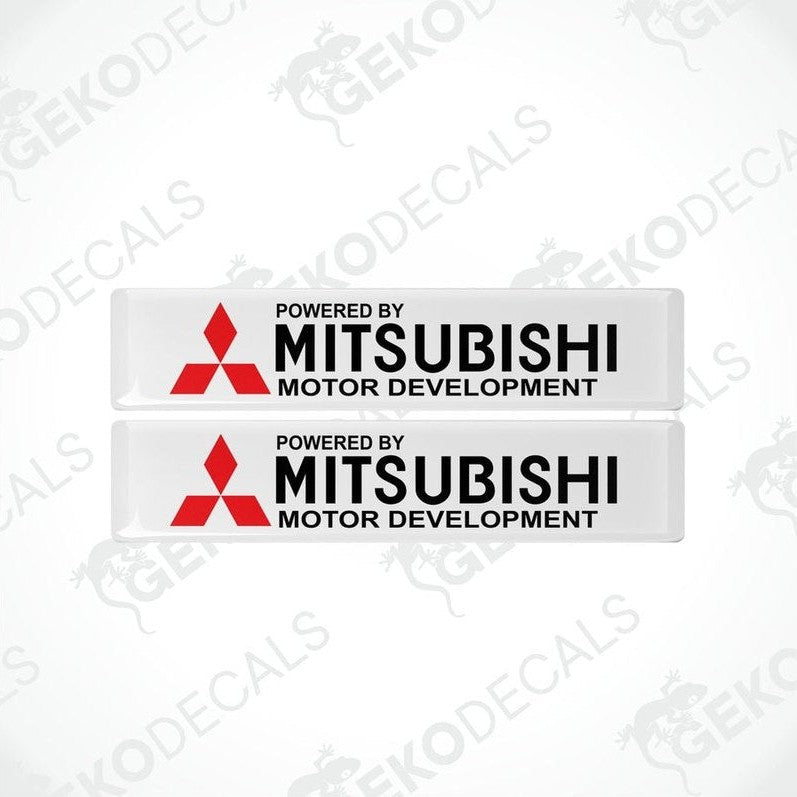 Two rectangular white vinyl decals with the red Mitsubishi logo and the text 'POWERED BY MITSUBISHI MOTOR DEVELOPMENT'.