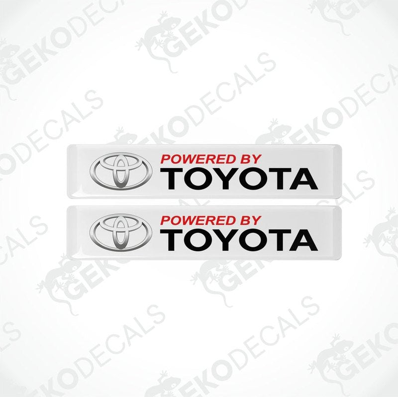 Two withe vinyl stickers with the text 'POWERED BY TOYOTA' in red and black Toyota logo.