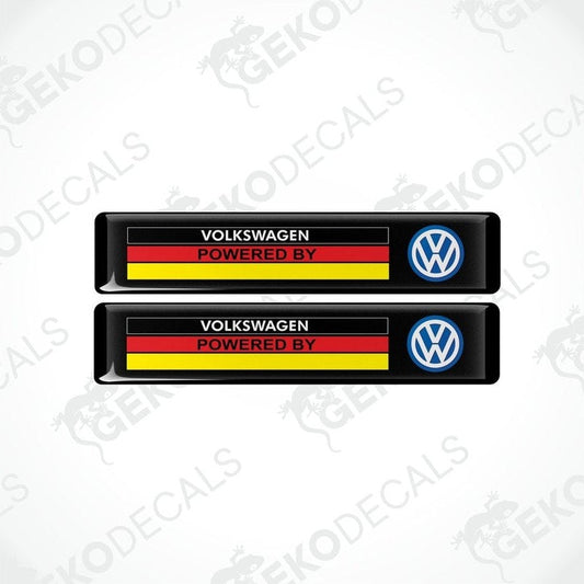 Two black vinyl stickers with the text 'Volkswagen POWERED BY' and a flag pattern in red and yellow and a blue logo on a white background.