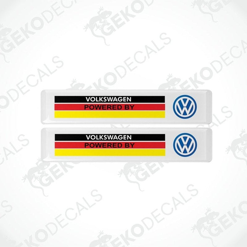 Two withe vinyl stickers with the text 'Volkswagen POWERED BY' and a flag pattern in red and yellow and a blue logo on a white background.