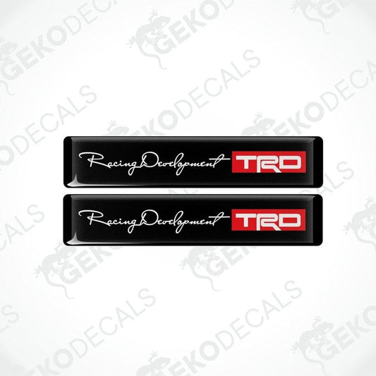 Two black vinyl decals with white and red text and logos, one decal reads 'Racing Development' and the other has 'TRD' logo.