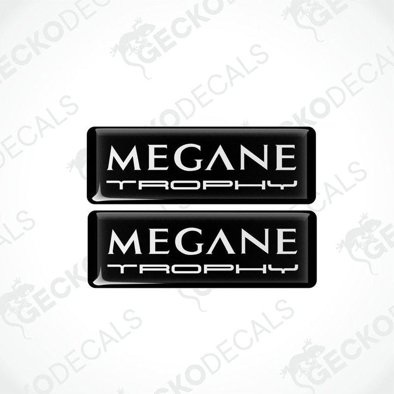 Two black rectangular vinyl decals with 'MEGANE TROPHY' white text on them, intended for use as car stickers.