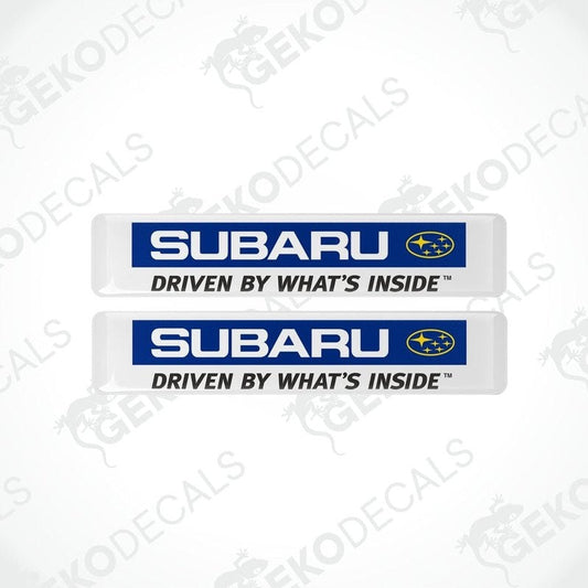 Two white vinyl stickers with the Subaru brand logo and the slogan 'DRIVEN BY WHAT'S INSIDE' printed in blue and yellow.