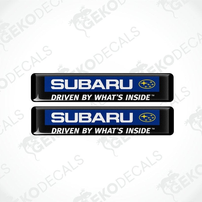 Two black rectangular decals with the Subaru logo and the text 'DRIVE BY WHAT"S INSIDE.
