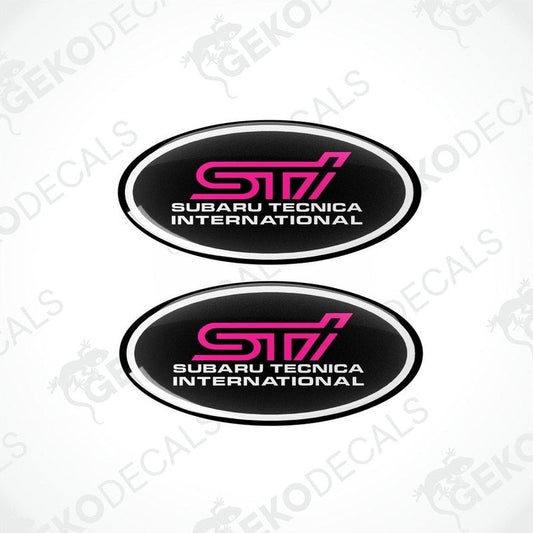 Two oval-shaped decals with 'STI SUBARU TECNICA INTERNATIONAL' text in pink on a black background.