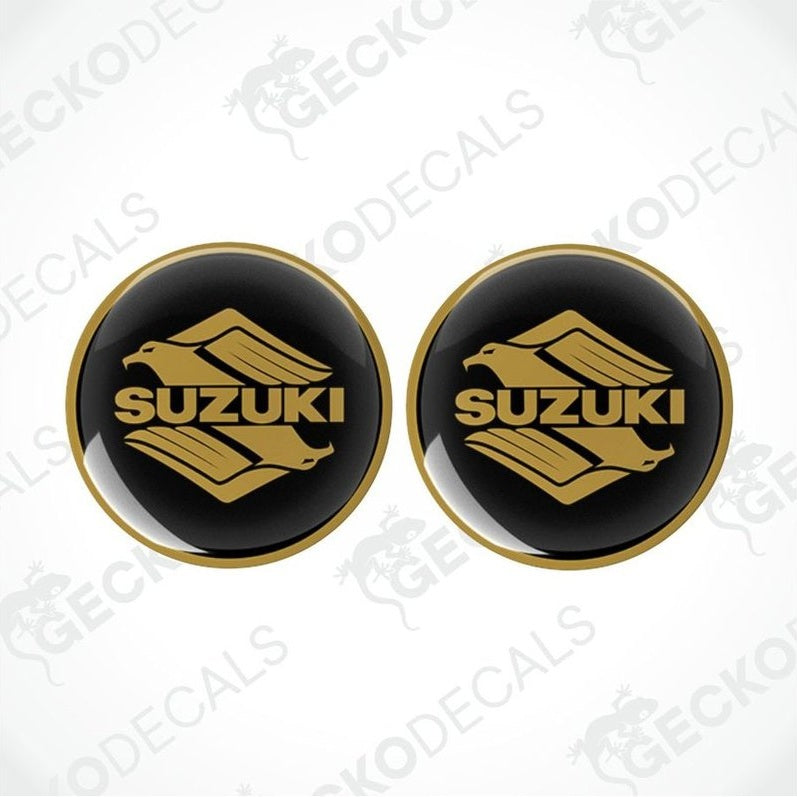 Two round black stickers with gold Suzuki logo on a white background.