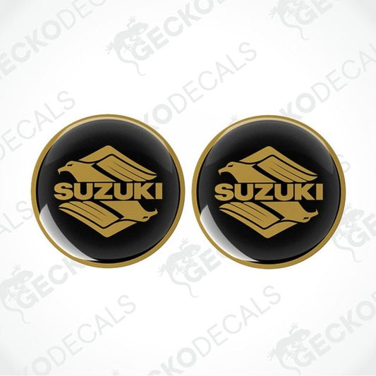 Two round black stickers with gold Suzuki logo on a white background.