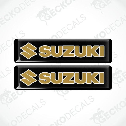 Two Suzuki logos in gold on black rectangles with a white background.