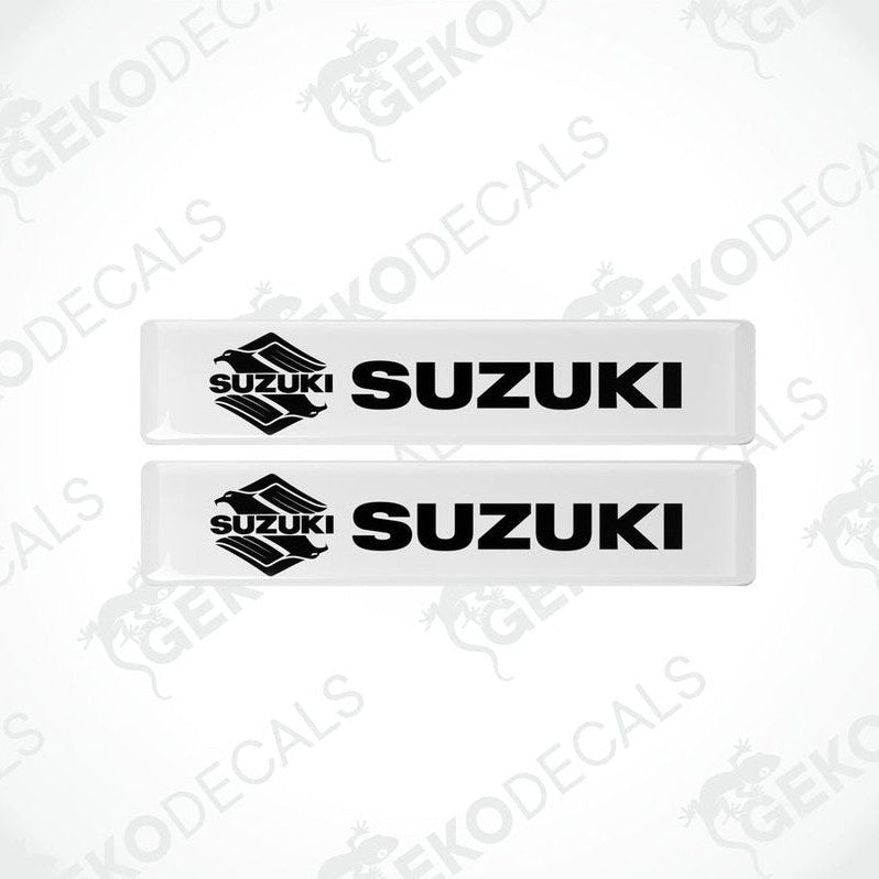 Two withe vinyl stickers with the word 'SUZUKI' printed on them.