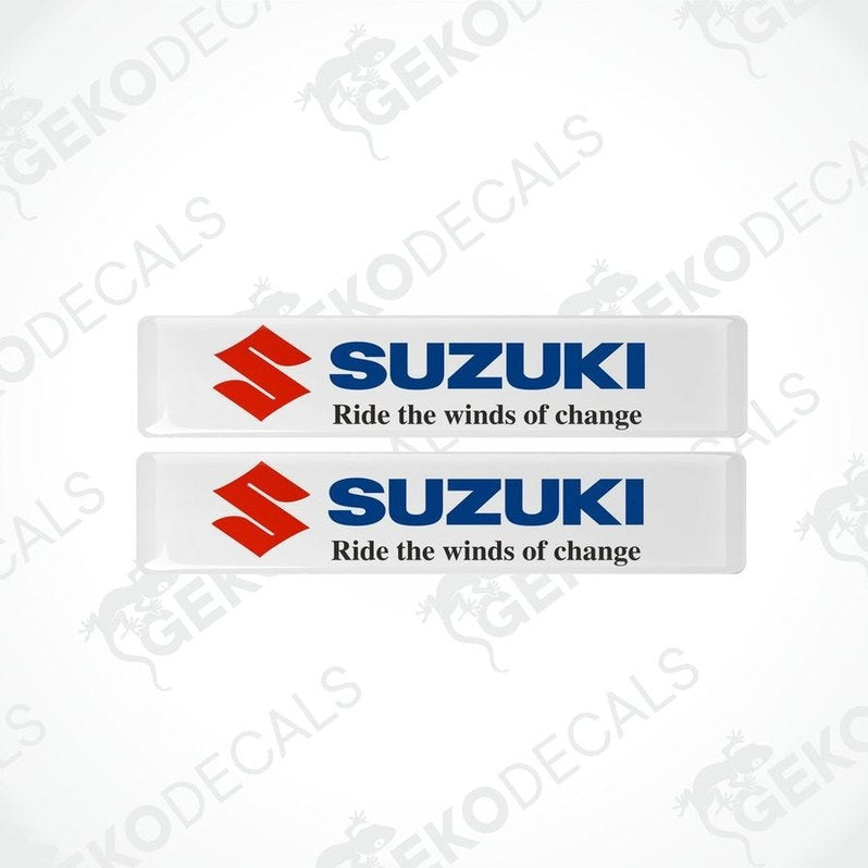 Two white rectangular vinyl decals with the SUZUKI logo and the phrase 'Ride the winds of change' printed on them.