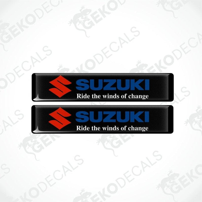 Two black rectangular vinyl decals with the SUZUKI logo and the phrase 'Ride the winds of change' printed on them.