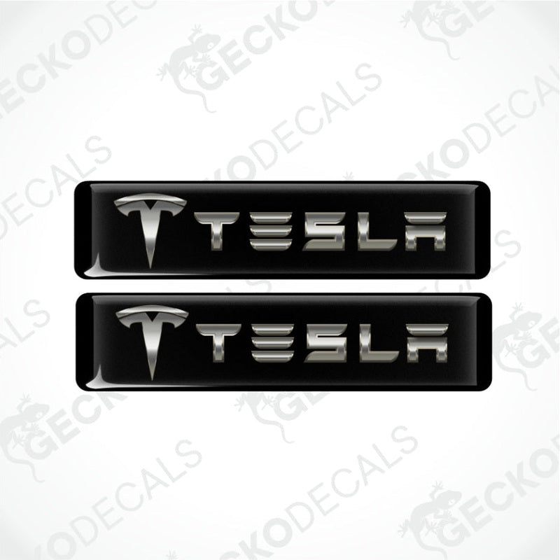 two dimensional metallic Tesla logo with emblem in front on a black background