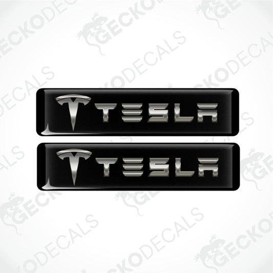 two dimensional metallic Tesla logo with emblem in front on a black background