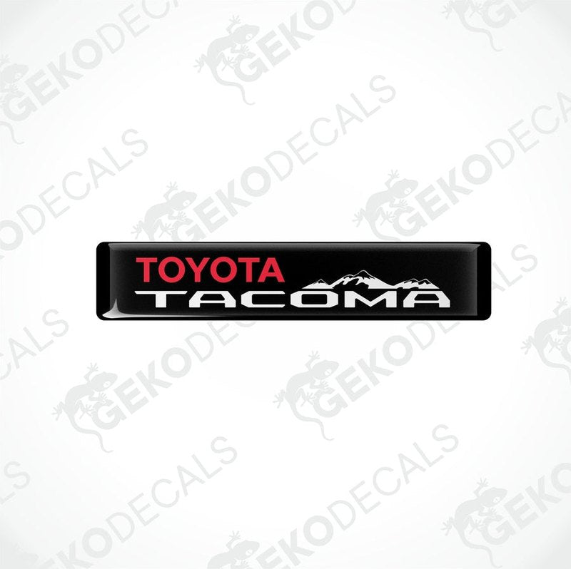 Black vinyl decals with red and white text 'TOYOTA TACOMA' and a mountain range image.