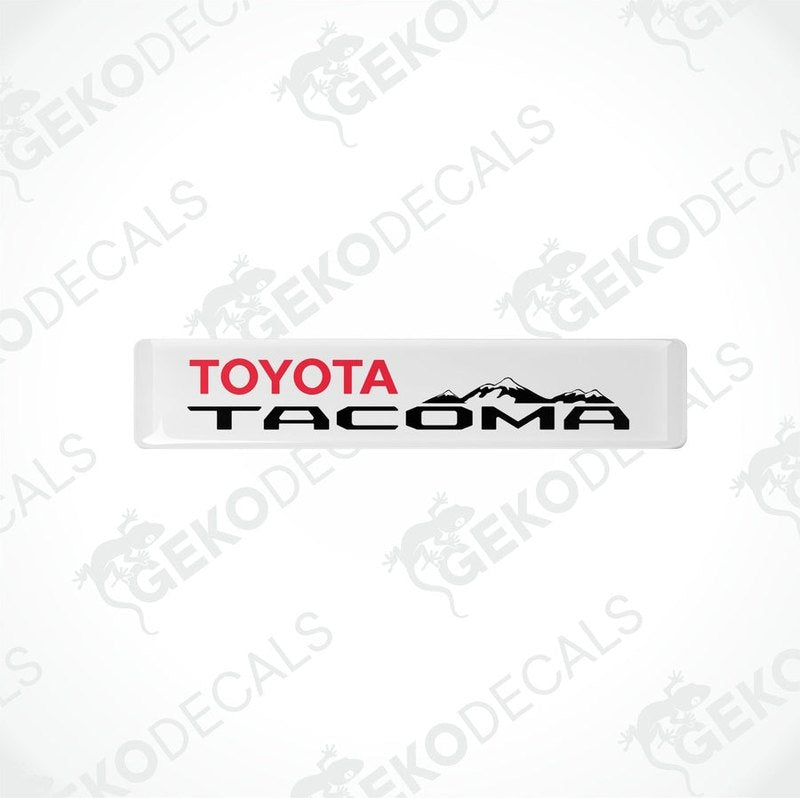 Withe vinyl decals with red and black text 'TOYOTA TACOMA' and a mountain range image.