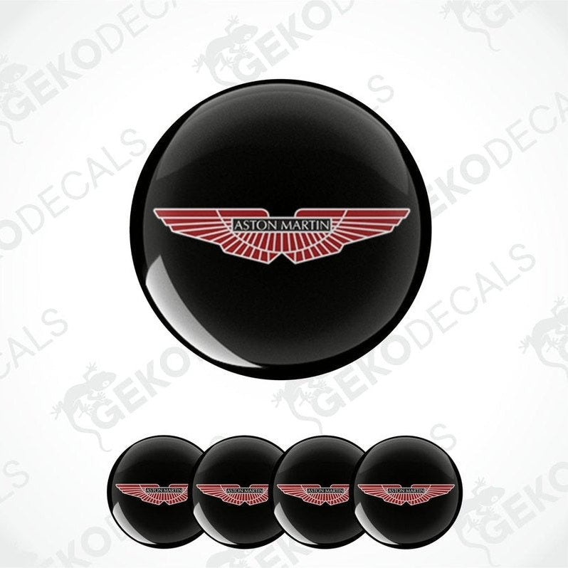 A set of vinyl decals with the Aston Martin logo applied on black circular surfaces, likely for vehicle wheels.
