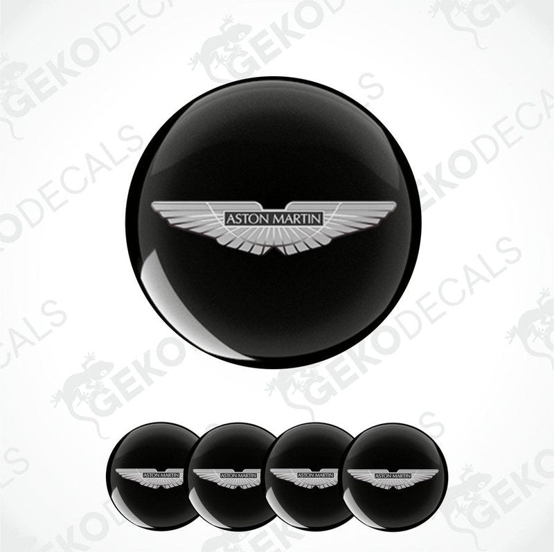 A set of vinyl decals with the Aston Martin logo applied on black circular surfaces, likely for vehicle wheels.