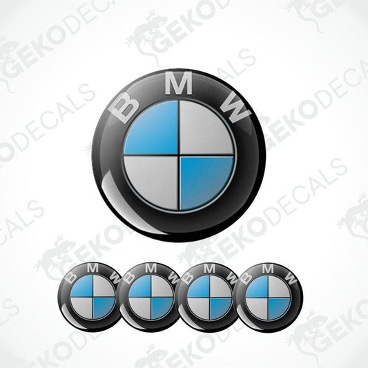 A set of four BMW emblem stickers, with one large emblem in the center and three smaller ones around it, all in black, blue, and white colors.