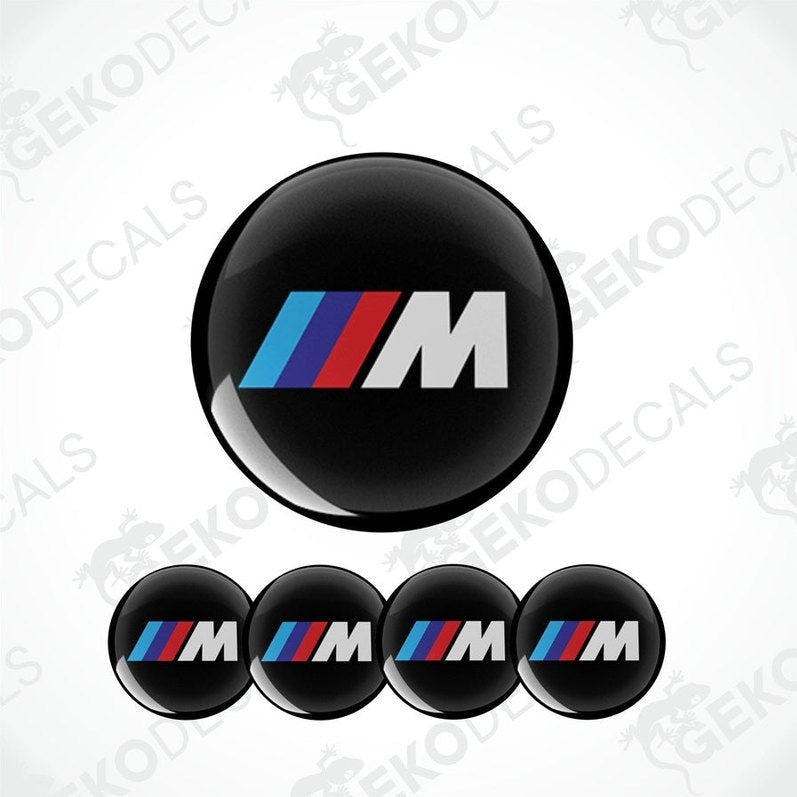 A set of four round car decals with a black background featuring a red and blue striped 'M' logo.