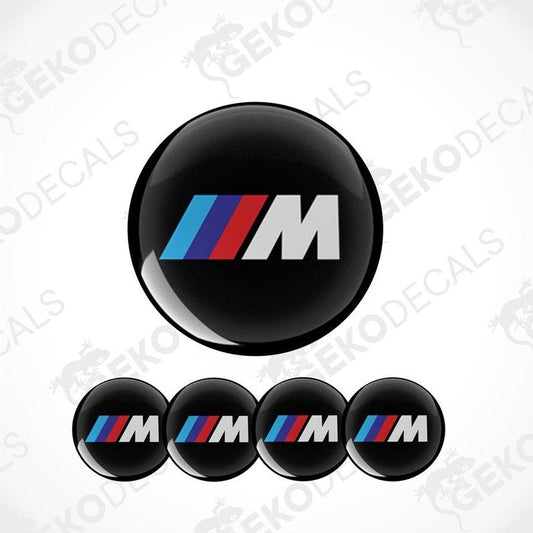 A set of four round car decals with a black background featuring a red and blue striped 'M' logo.