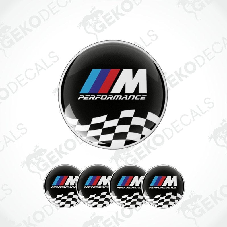 A set of four black vinyl stickers with the BMW M PERFORMANCE logo in white. The stickers have a checkered pattern with a white border and the BMW logo in the center.