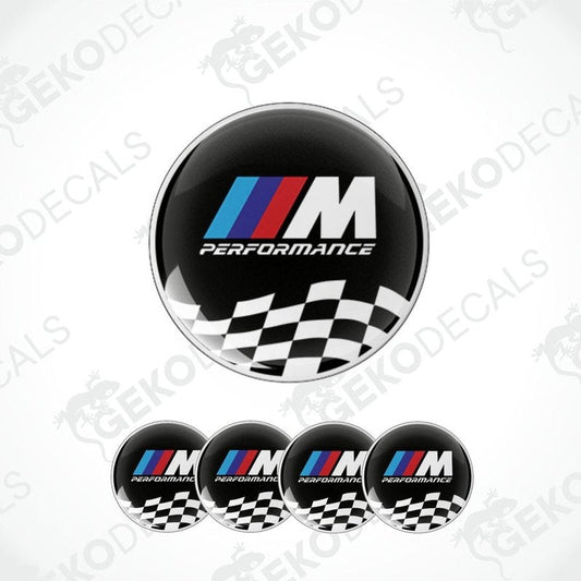 A set of four black vinyl stickers with the BMW M PERFORMANCE logo in white. The stickers have a checkered pattern with a white border and the BMW logo in the center.