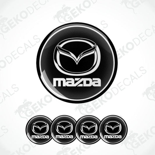 A set of black and white vinyl decals with the Mazda logo, including four different sizes shown against a white background.
