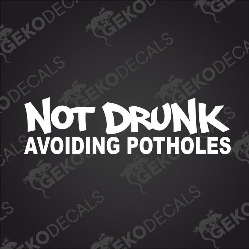 White die cut car decal with 'NOT DRUNK AVOIDING POTHOLES' text on dark background