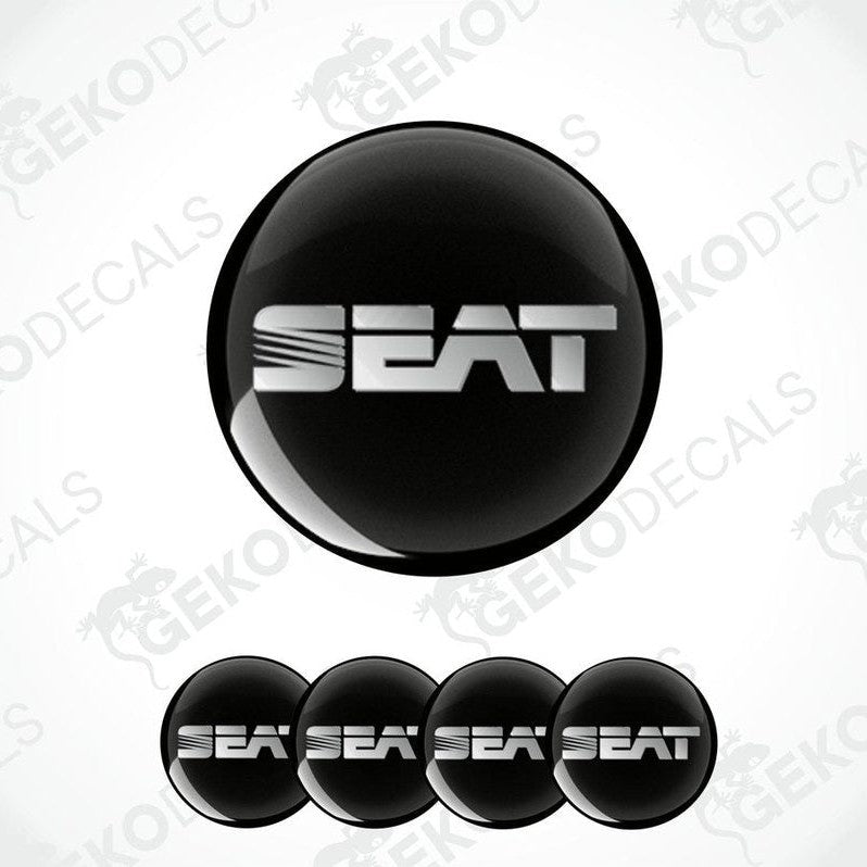 
A set of round car stickers with the brand name "SEAT" written in silver in block letters, mainly in black with a glossy finish.