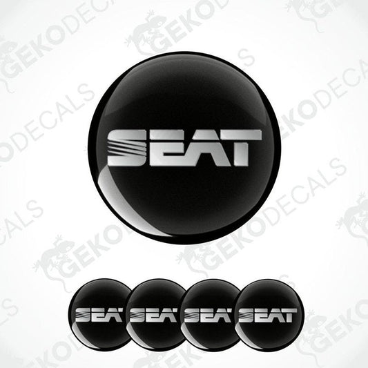 
A set of round car stickers with the brand name "SEAT" written in silver in block letters, mainly in black with a glossy finish.
