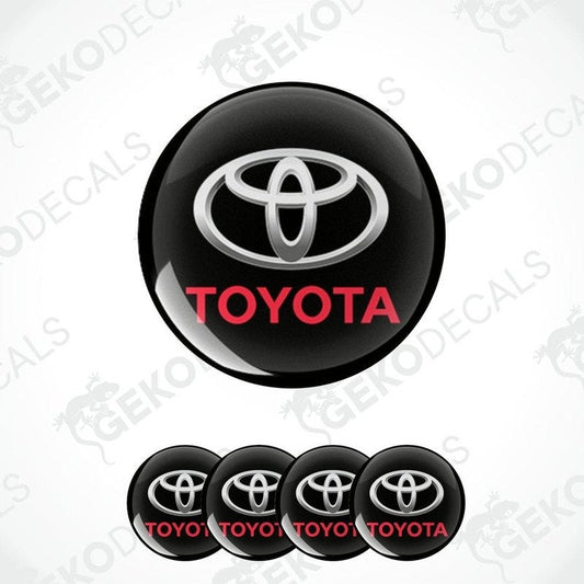 A set of black, white, and red Toyota wheel decals. The main decal is circular with the Toyota logo in white and red on a black background.