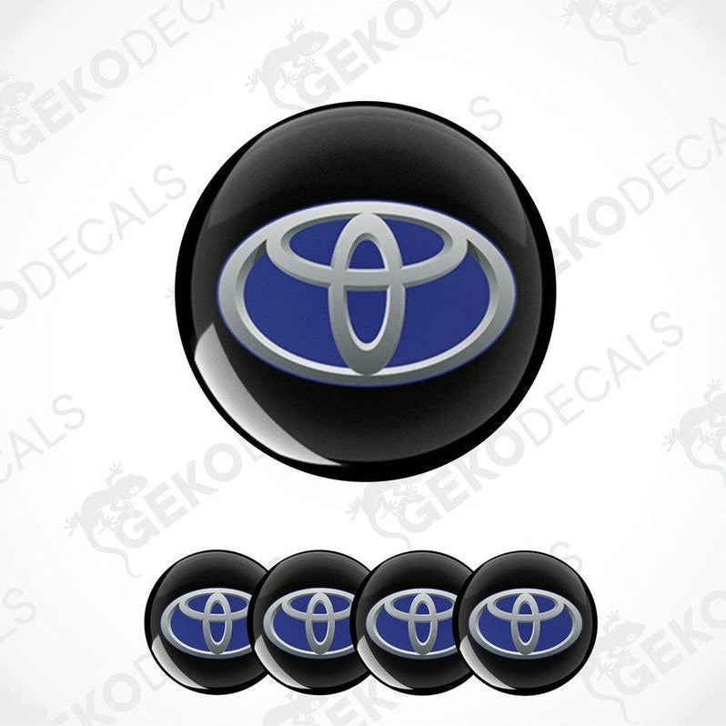 A set of four vinyl stickers with a Toyota brand logo, including two in black with a blue and silver Toyota emblem, and two in gray with a blue and silver Toyota emblem.